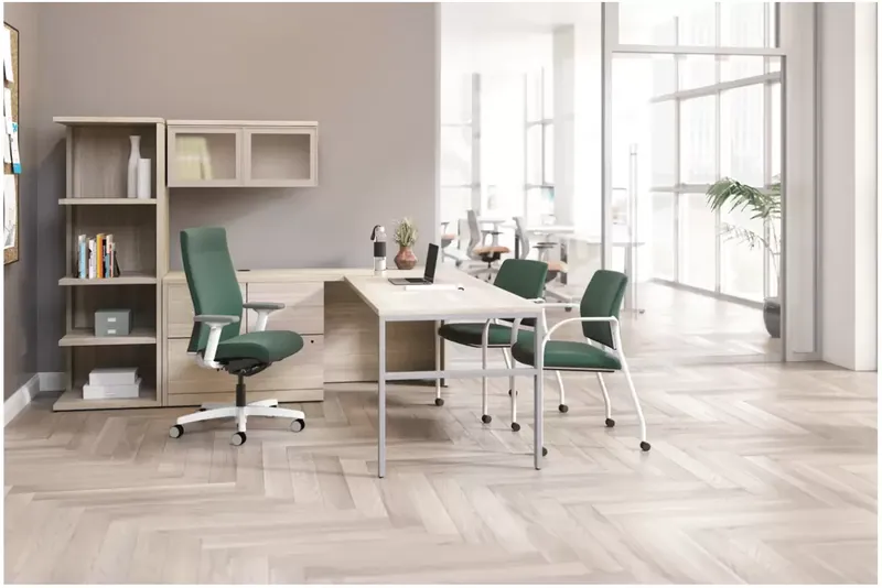 Light wood desk and storage with green office and guest chairs beside large windows.